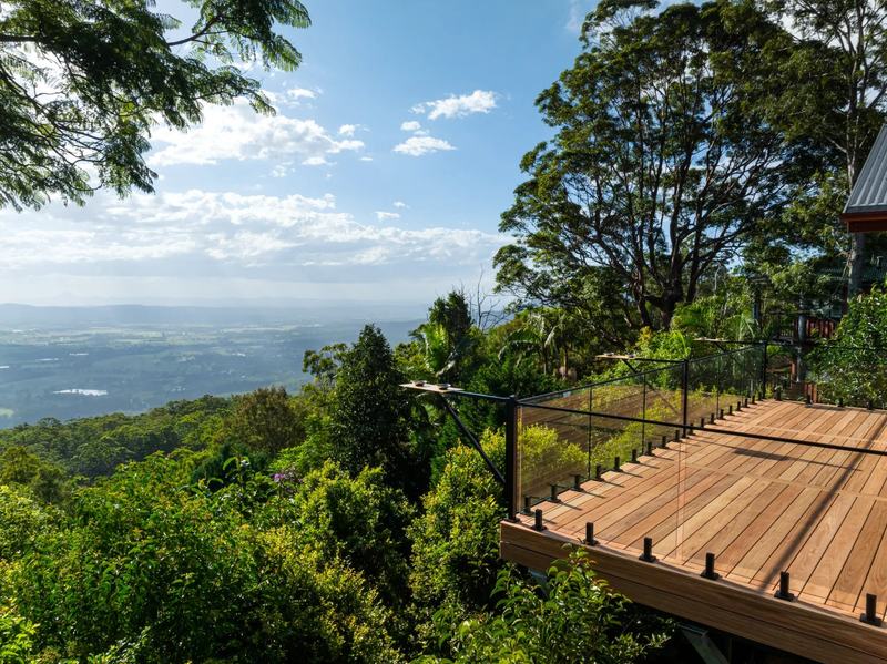 A high-set timber deck with wire balustrade cantilevered over a forested hinterland valley.