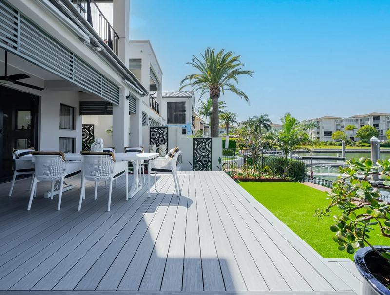 A low-set grey composite deck running alongside a house to a lawn and canal.